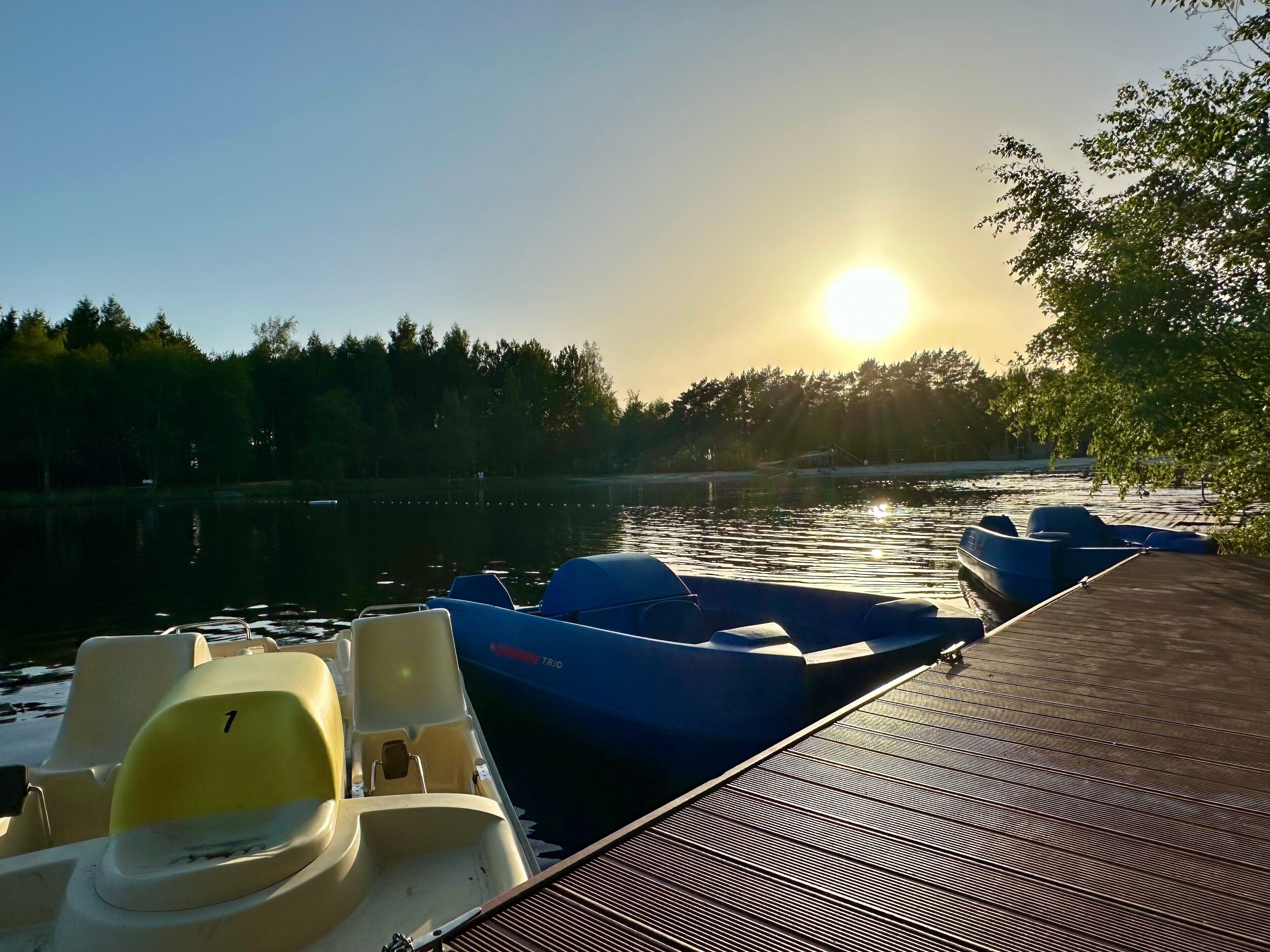 A dock with boats, a calm body of water, and a sunset in the background.