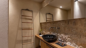A bathroom with a wooden vanity, a black basin, and a stone backsplash. - Korona Boutique Hotel - Deluxe Room (Oitylo)