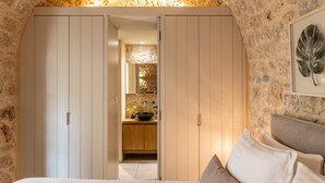 A bedroom with a bed, a nightstand, a large window, and a stone wall. - Korona Boutique Hotel - Deluxe Room (Oitylo)