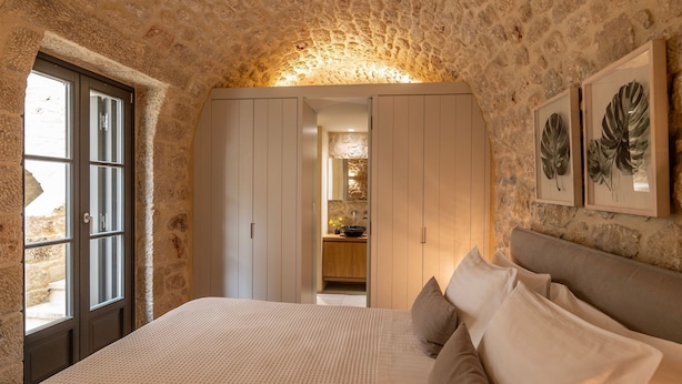 A bedroom with stone walls, a bed with pillows, a wardrobe, and a framed plant. - Korona Boutique Hotel - Deluxe Room (Oitylo)