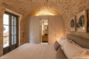 A bedroom with stone walls, a bed with pillows, a wardrobe, and a framed plant.
