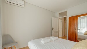 A hotel room with a bed, a chair, an air conditioning unit, and a door leading to another room. - Apartment  by Interhome (Porto)