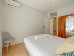 A hotel room with a bed, a chair, an air conditioning unit, and a door leading to another room. - Apartment  by Interhome (Porto)