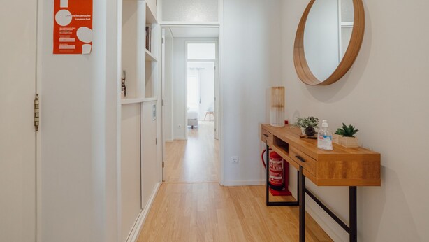 A hallway with a wooden floor, a wooden console table with a mirror, a fire extinguisher, and a door leading to a bedroom. - Apartment  by Interhome (Porto)