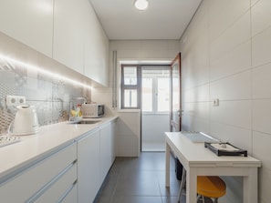 Et moderne køkken med hvide skabe, en indbygget mikrobølgeovn og en elkedel.
