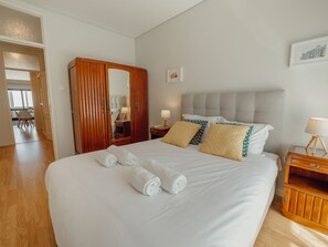 Habitación de hotel con una cama grande, un armario de madera, una mesita de noche con lámpara y vistas al pasillo.