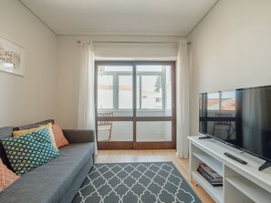 A living room with a sofa, a flat-screen TV, a bookshelf, and a sliding glass door leading to a balcony. - Apartment  by Interhome (Porto)