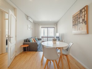 Una sala de estar moderna con un sofá, una mesa de comedor con sillas, una mesita auxiliar y un gran ventanal con cortinas.