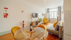 Un salon moderne avec une table à manger en verre, des chaises jaunes, un canapé, un téléviseur et un extincteur fixé au mur.