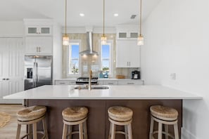 A modern kitchen with white cabinetry, a large island with stools, stainless steel appliances, and pendant lighting. - Expansive Home in PSJ Beach, 3 Kitchens/Living and Dining areas! Private Pool (St. Joe Beach)