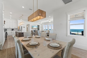 A modern kitchen with white cabinets, a stainless steel refrigerator, and a dining area with a wooden table set for six. - Expansive Home in PSJ Beach, 3 Kitchens/Living and Dining areas! Private Pool (St. Joe Beach)