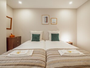 Un lit double avec une parure de lit à rayures, deux oreillers, une table de chevet avec une lampe et une commode sur laquelle est posé un vase.