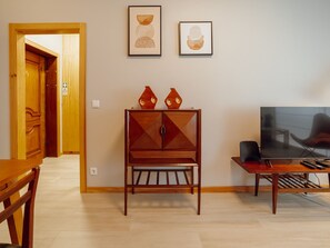 A living room with a wooden cabinet, two framed artworks, a television, and a dining table with chairs. - GOOD MORNING APARTMENT with GARAGE by VACATIONY by Interhome (Porto)