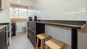 Una cuina moderna amb taulell negre, tamborets de fusta, una finestra i vista cap a l'exterior.