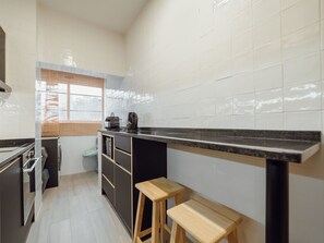 A modern kitchen with a black countertop, wooden stools, a window, and a view of the outside. - GOOD MORNING APARTMENT with GARAGE by VACATIONY by Interhome (Porto)
