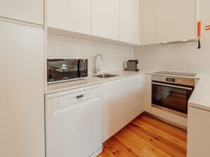 Eine kleine Küche mit weißen Schränken, einem Geschirrspüler, einer Mikrowelle, einer Kaffeemaschine und einem Backofen.