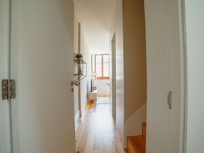 Un couloir avec un plancher en bois, une porte à gauche et une fenêtre à droite.