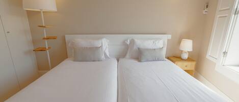Una cama doble con sábanas blancas, una mesita de noche con lámpara y un aplique de pared.