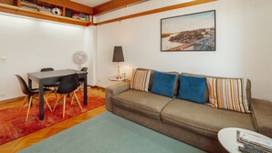 Ein Wohnzimmer mit einer Couch, einem Esstisch mit Stühlen, einer Lampe und einem Bild an der Wand.