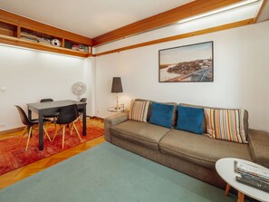 Ein Wohnzimmer mit einer Couch, einem Esstisch mit Stühlen, einer Lampe und einem Bild an der Wand.