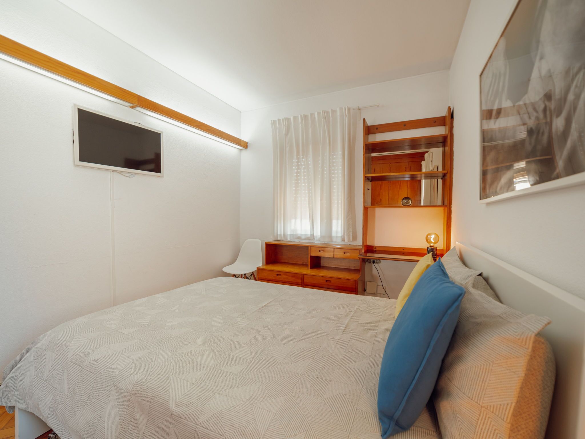 Ein Schlafzimmer mit einem Bett, einem Schreibtisch, einem Stuhl, einem Fernseher und einem Fenster mit Vorhängen.