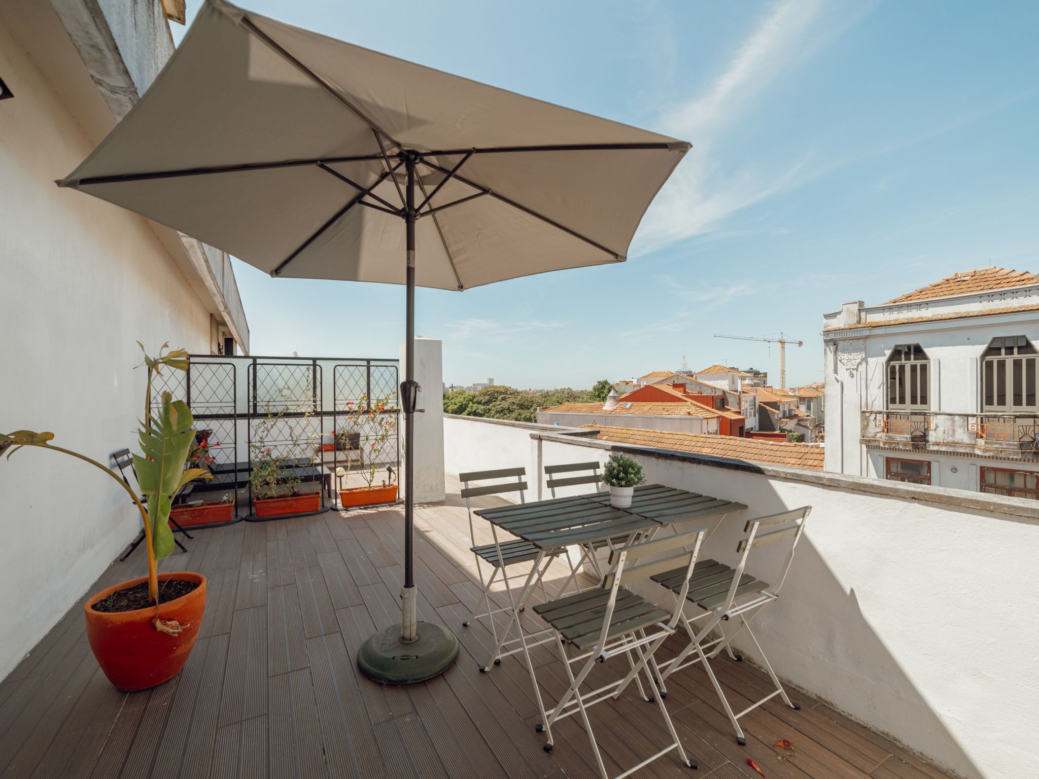 Una terrazza sul tetto con un tavolo, sedie, una pianta in vaso e un ombrellone grande.