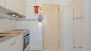 Eine kleine Küche mit weißen Schränken, einem eingebauten Backofen, einer Holz Arbeitsplatte und einer gefliesten Spritzschutzwand.