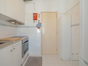 Eine kleine Küche mit weißen Schränken, einem eingebauten Backofen, einer Holz Arbeitsplatte und einer gefliesten Spritzschutzwand.