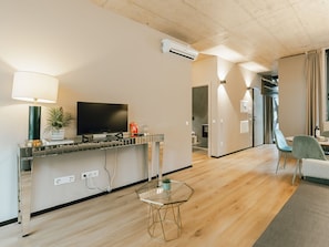 Een moderne woonkamer met een flatscreen televisie, een koffieapparaat en een kleintje tafel met een plant.