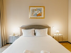 Hotellihuone, jossa on suuri sänky, kaksi yöpöytää, taulu seinällä ja verho vasemmalla puolella.