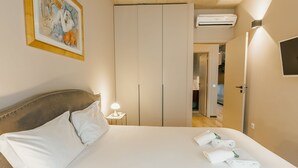 Hotellihuone, jossa on sänky, yöpöytä lampun kanssa, vaatekaappi ja seinälle asennettu televisio.