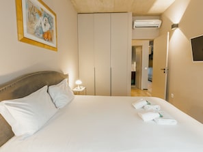 A hotel room with a bed, a nightstand with a lamp, a wardrobe, and a television mounted on the wall. - Apartment  by Interhome (Porto)