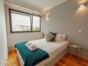 A hotel room with a bed, a window, a bedside table, and a wall-mounted light. - Apartment  by Interhome (Porto)