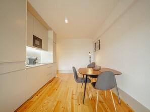 A modern kitchen with white cabinets, a microwave, and a wooden dining table with four chairs. - Apartment  by Interhome (Porto)