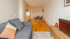 A modern living room with a sofa, a dining table with chairs, and a wooden side table with a vase. - Apartment  by Interhome (Porto)