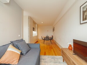 Uma sala de estar moderna com um sofá, uma mesa de jantar com cadeiras e uma mesinha de madeira com um vaso.