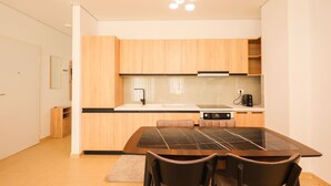 A modern kitchen with wooden cabinets, a black countertop, and a dining table with chairs. - SanPietro Vacation Apartment 050 (Plazhi San Pietro)