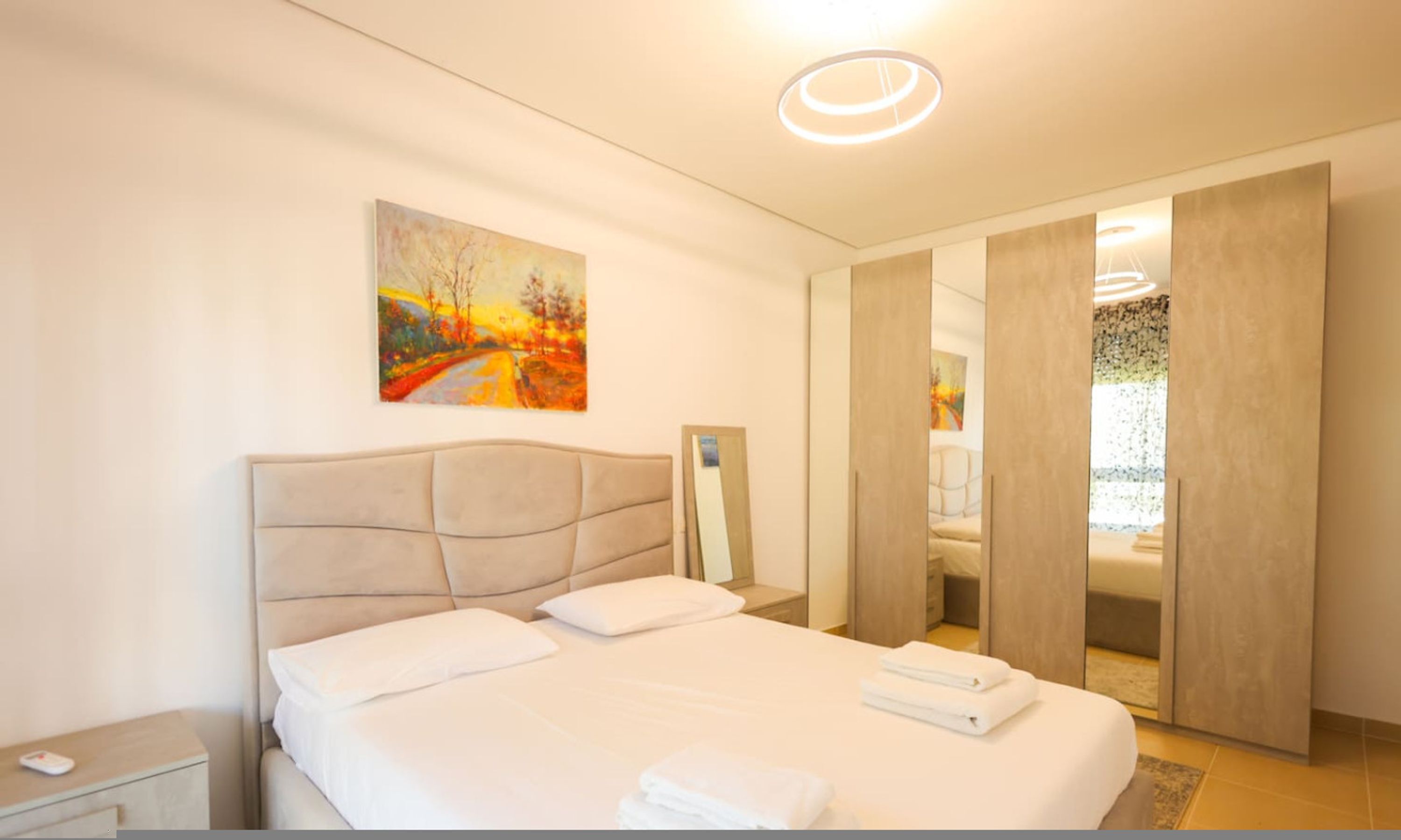 Ein modernes Schlafzimmer mit einem großen Bett, einem Nachttisch, einem Gemälde an der Wand und einem Spiegel.