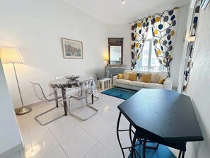 Een moderne woonkamer met een bank, een eettafel met stoelen, een open haard en een groot raam met gordijnen.