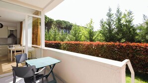 A balcony with a table and chairs, a view of a hedge, and a glimpse of a kitchen. - Lura Apartment 05 in Plazhi San Pietro (Plazhi San Pietro)
