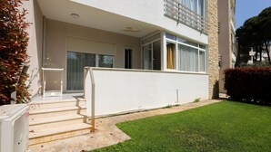 A two-story building with a white exterior, a balcony on the upper floor, and a small front yard with a lawn and steps leading to the entrance. - Lura Apartment 05 in Plazhi San Pietro (Plazhi San Pietro)