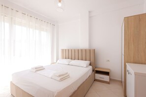 A hotel room with a large bed, a nightstand, a wooden wardrobe, and a window with sheer curtains. - Sunny Apartment, Balcony & Beach Access (Plazhi San Pietro)