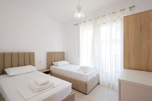 Camera d'albergo con due letti, un armadio in legno, una finestra con tende leggere e un moderno lampadario.