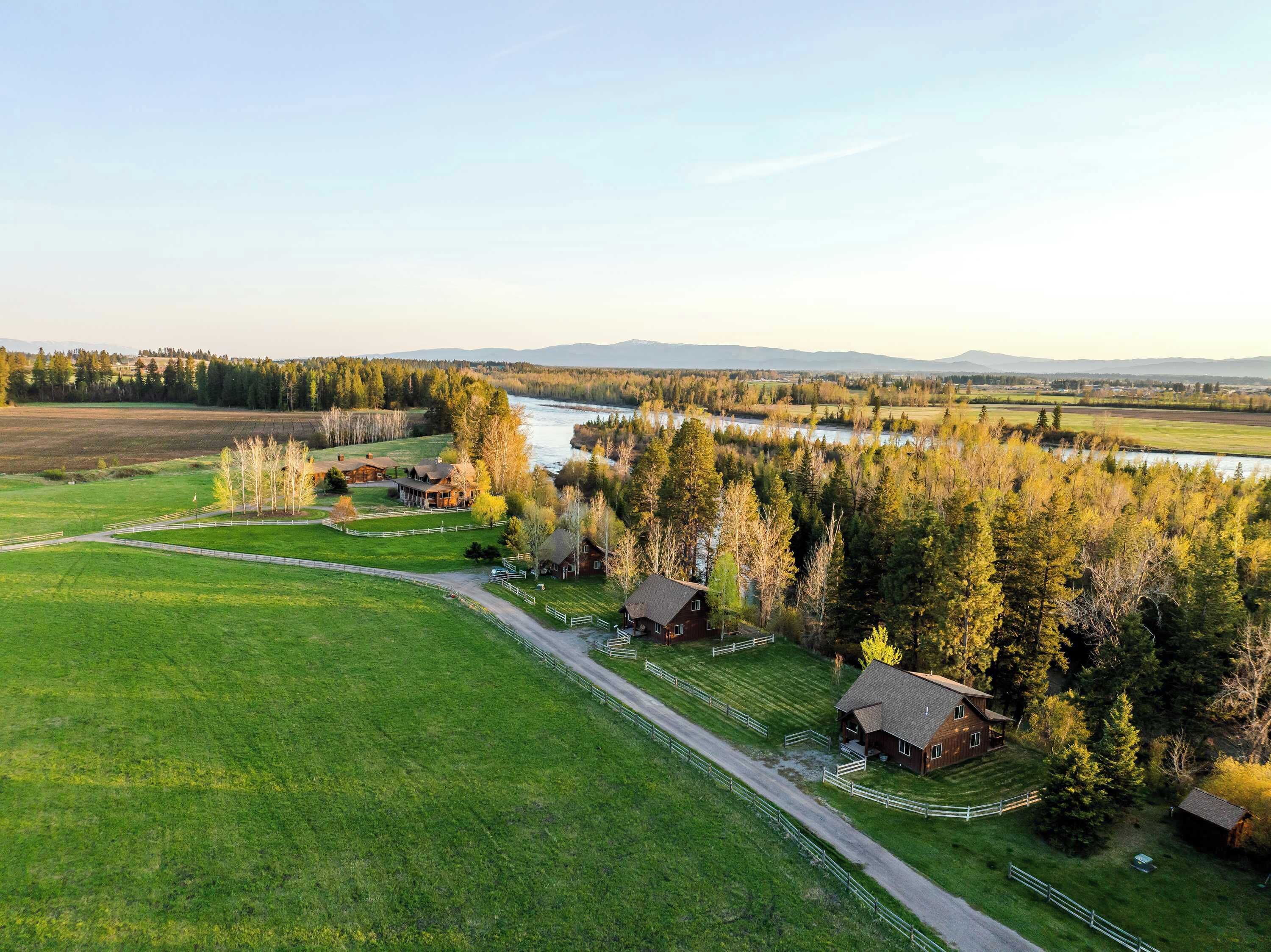 A rural landscape with a river, fields, and wooden cabins.