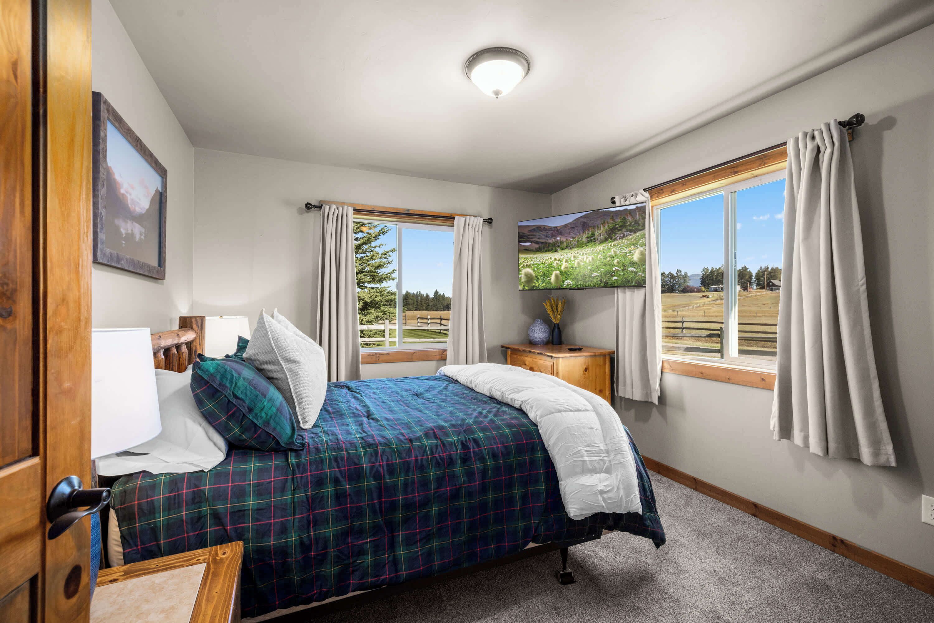A bedroom with a bed, a TV, a window with curtains, and a wooden door.