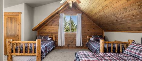 Una habitación con dos camas de madera, un ventilador de techo y una ventana con cortinas.
