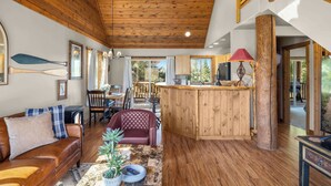 Interior em madeira com sofá, área de refeições e bancada de cozinha.