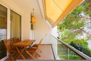 A balcony with a wooden table and chairs, a hanging light fixture, and a view of greenery. - Boho-Chic Apartment with Garden Views (Plazhi San Pietro)