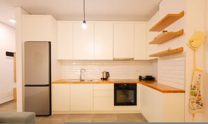 Eine moderne Küche mit weißen Schränken, einem Edelstahlkühlschrank, einem Geschirrspüler und Holzregalen.