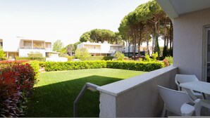 A courtyard with a lawn, white chairs, and a building with balconies. - Lura Apartment 04 in Plazhi San Pietro (Plazhi San Pietro)